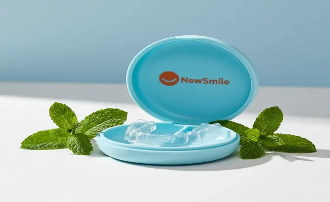 NewSmile night guard in its case, styled beside fresh mint leaves and a soft blue backdrop.